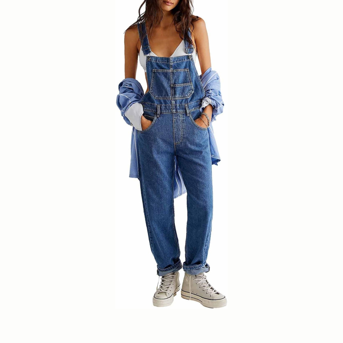A model wearing blue denim overall-style pants with a white tank top, a light blue button-up shirt draped off the shoulders, and white high-top sneakers, photographed against a plain white background.