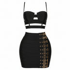 A two-piece black outfit featuring a strappy bandeau-style crop top and a high-waisted bodycon mini skirt with gold-tone buckle detailing along the side, shown on a plain white background.