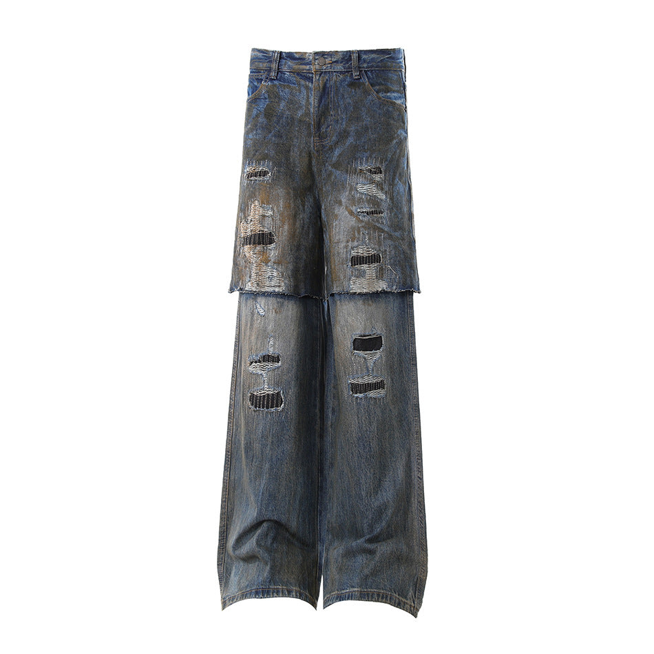 Distressed wide-leg denim pants in a faded blue wash with heavy rips and patches, shown flat against a white background.
